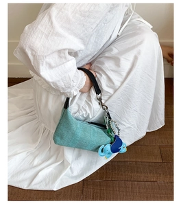 Detail of mint green woven dumpling bag with black leather handle and blue elephant charm