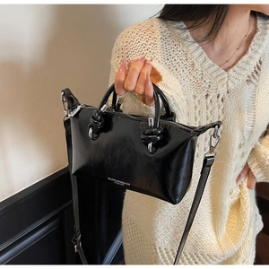 Detail of glossy black leather handbag showing knotted handles and brand logo texture