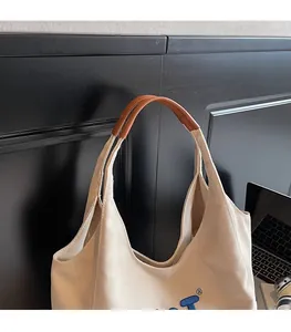 Close-up of durable canvas tote with brown leather handles and blue embroidery details