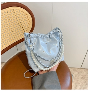 Détail du sac seau bleu clair avec chaîne de perles et breloque étoile sur fauteuil