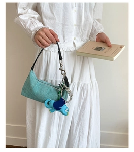 Close-up of light green woven underarm bag with blue elephant charm and heart chain