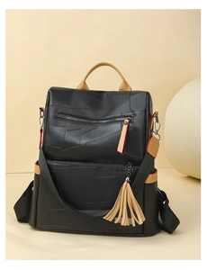 Close-up of black patchwork leather backpack with brown trim and stylish fringe tassel