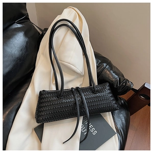 Detail shot of black woven faux leather baguette bag on a white blazer background