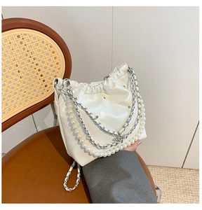 Détail du sac seau blanc matelassé avec bandoulière en perles et chaîne argentée sur une chaise