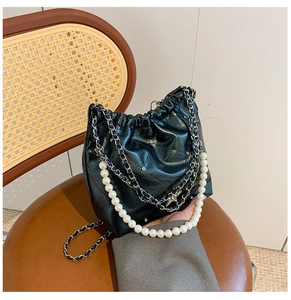 Détail du sac seau noir brillant avec poignée perlée et bandoulières en chaîne