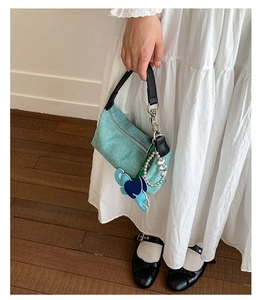 Detail of mint green woven tote with black leather handle and elephant charm