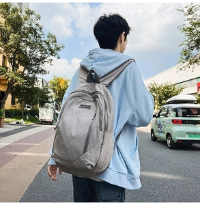 Outdoor street shot of a light grey nylon backpack with textured pleats on male model