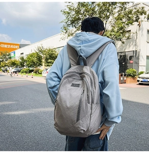 Outdoor view of a grey minimalist backpack showing the padded shoulder straps and zippers