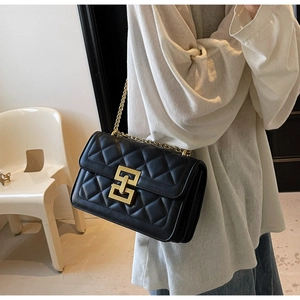 Détail d'un sac bandoulière matelassé noir avec chaîne dorée et fermoir entrelacé