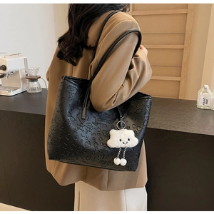 Dettaglio borsa tote in pelle nera goffrata con motivi cartoon e ciondolo a nuvola