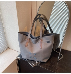Detail of dark grey canvas tote bag with brown handles and blue stitching accents