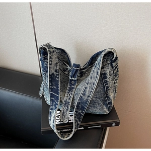 Detail of acid wash denim tote bag featuring silver eyelets and wide adjustable strap