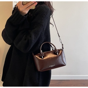Detail view of deep brown glossy leather texture and round handle on the crossbody bag