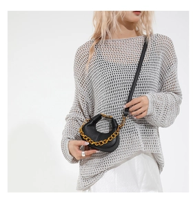 Detail of a black pebbled leather half-moon bag with gold chain handle on model