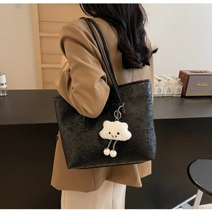 Dettaglio della borsa tote nera in pelle con motivi a rilievo e ciondolo a nuvola di peluche