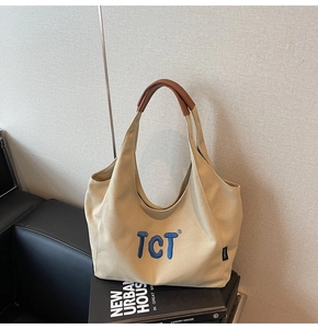 Detail of beige canvas tote bag with blue TCT embroidery and brown leather handle