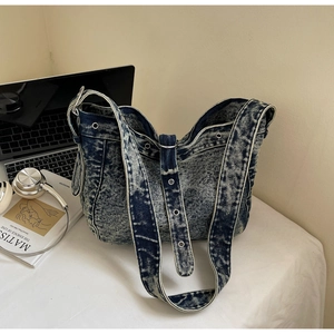 Detail of acid-wash denim tote bag with metal eyelets on shoulder strap in a desk setting