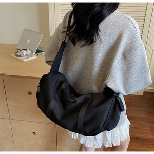 Dettaglio di una borsa a tracolla nera in nylon capiente con tracolla larga su scrivania