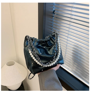 Détail du sac seau noir matelassé avec une élégante chaîne en perles et métal argenté