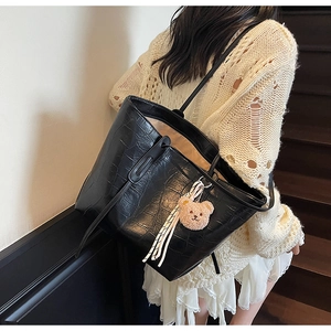 Detail of black faux crocodile leather tote bag with plush bear charm and striped ribbon decoration