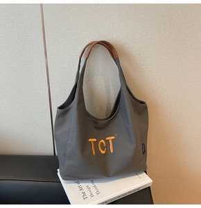 Detail of grey canvas tote bag with yellow TCT embroidery and brown leather handle