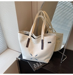 Detail of canvas tote bag with dark brown leather accents and blue X-shaped stitching