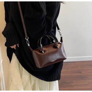 Detail of a dark brown glossy leather crossbody bag worn with a casual fashion outfit