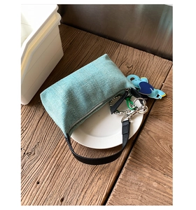 Detail of mint green knit dumpling bag with leather strap and blue elephant charm