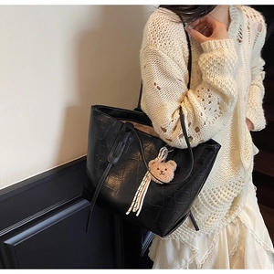 Detail of black faux crocodile leather tote bag with plush bear charm on white outfit