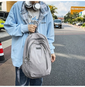 Outdoor street view of a high-capacity light gray nylon backpack with zipper pockets