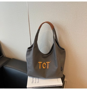 Close-up of grey canvas tote with yellow TCT embroidery and brown leather handles