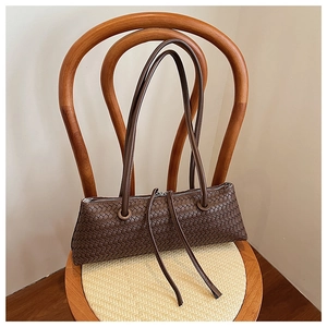 Detailed view of dark brown woven leather baguette shoulder bag on a vintage wooden chair