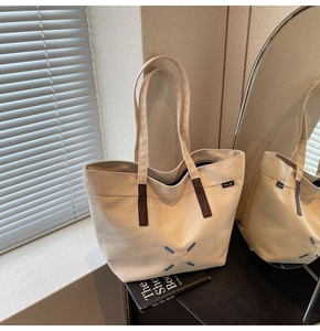 Detail of canvas tote bag with brown leather accents and blue X stitching pattern