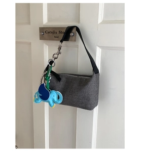 Detailed view of grey woven shoulder bag with a blue elephant charm on a white door