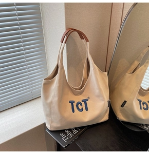 Detail of beige canvas tote with blue logo and brown leather handle on a dark table