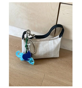 Detail of woven fabric handbag with black leather handles and blue elephant charm decoration