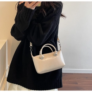 Detail of cream-white leather crossbody bag featuring unique knotted handle decoration