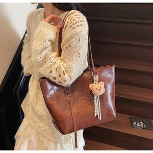 Detail of dark brown faux crocodile leather tote bag with a cute plush bear pendant charm