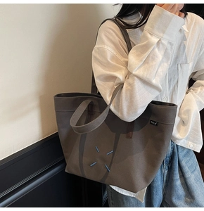 Detail of dark gray canvas tote bag featuring signature blue cross stitching and brand tag