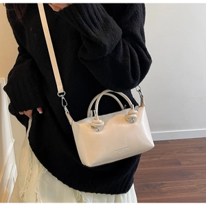 Detail showing the light beige glossy handbag with twisted knot handles and branding logo