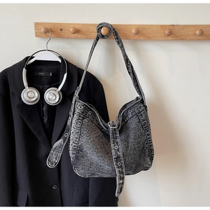 Close-up of washed denim tote bag with silver eyelets and buckle on a wooden hanger