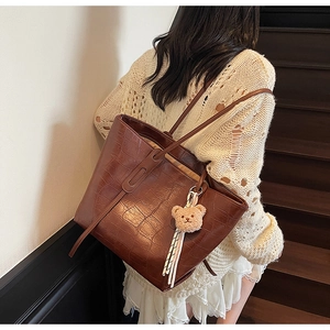 Detail of dark brown faux leather tote with crocodile pattern and plush bear charm