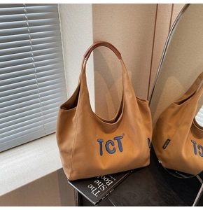 Detail view of khaki canvas tote with blue TCT embroidery and brown leather handle wrap