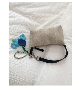 Detail of beige woven baguette bag with blue elephant charm and heart beads