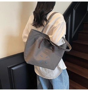 Detail of dark grey canvas tote bag with blue cross stitching and brown leather handles