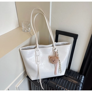 Detail of white crocodile pattern tote bag with a cute brown plush bear charm