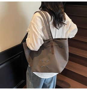 Detail of canvas tote bag with blue X-shaped stitching and leather strap reinforcement
