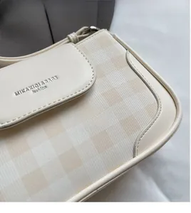 Detail der cremeweißen Tasche mit gelbem Schachbrettmuster und geprägtem Goldlogo