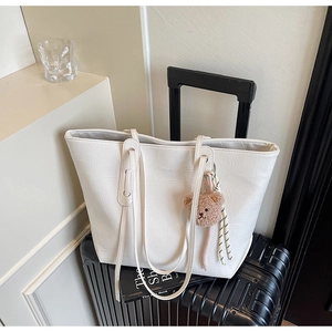 Detail of white crocodile texture tote bag with bear charm on a black suitcase