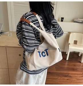 Detailed close-up of cream canvas tote bag with blue TCT embroidery and leather straps